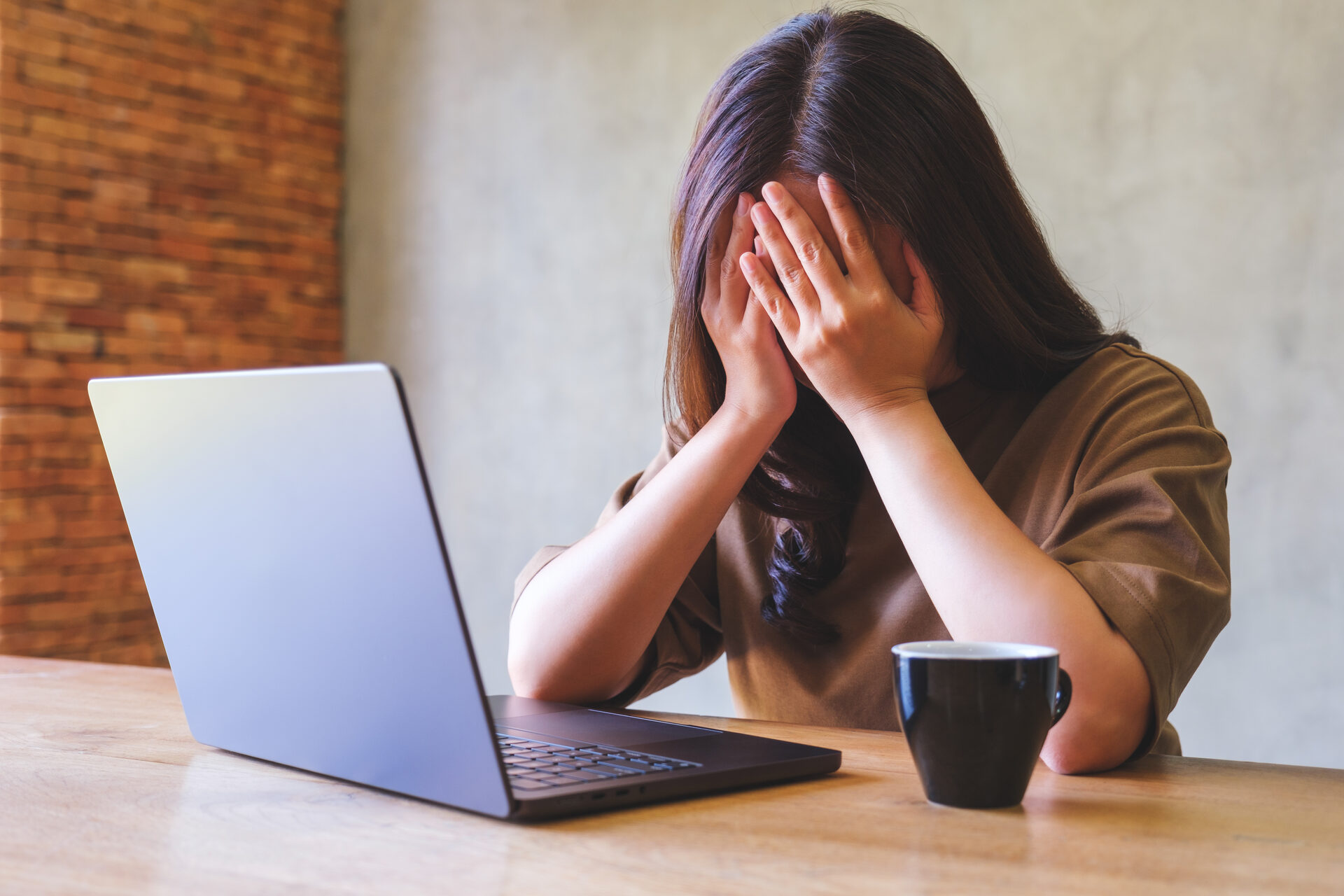 A user with her head in her hands at a laptop